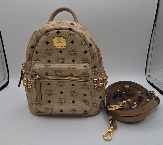 A beige MCM mini backpack with its matching detachable shoulder strap, displayed on a light gray studio background.